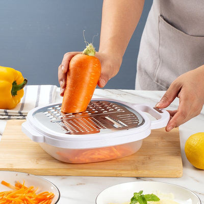 Multifunctional lunch box with stainless steel grater and white peeler slicing carrot on wooden board